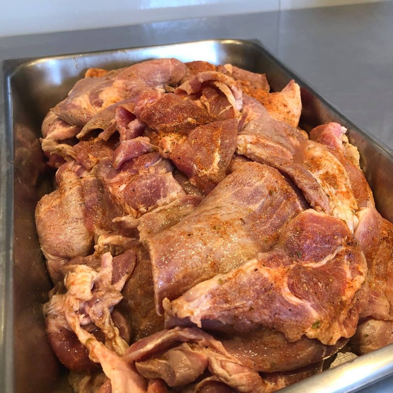 Seasoned raw pork shoulder pieces in a metal tray, ready for cooking at Townies Feel Good Food.