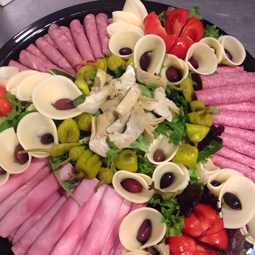A large platter of rolled deli meats, cheeses with olives, tomatoes, artichokes, and peppers.